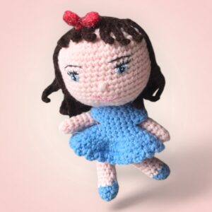 Adorable poupée au crochet avec une robe bleue et un nœud rose.