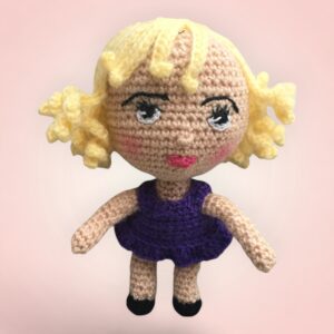 Petite poupée au crochet avec une jupe violette et des cheveux bouclés.