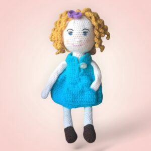 Poupée en crochet aux cheveux blonds frisés et portant une robe bleue.