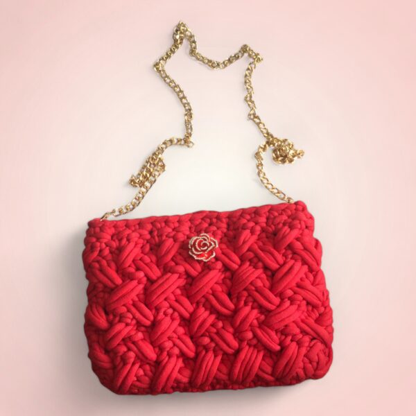 Sac à main rouge rectangulaire avec broche rose et chaîne dorée.