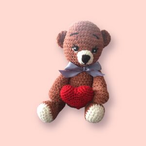 Adorable ours en crochet tenant un cœur rouge.