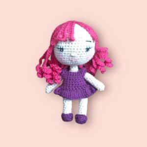 Poupée brune au crochet avec une robe violette et une chevelure rose.