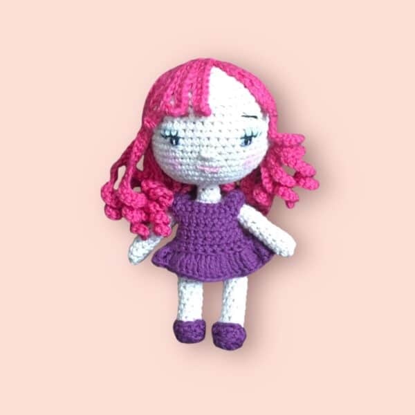 Poupée brune au crochet avec une robe violette et une chevelure rose.