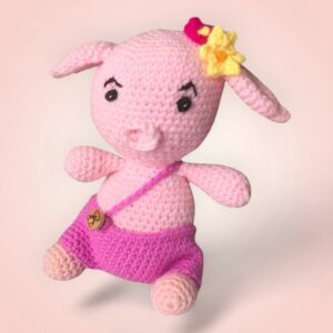 Charmant cochon rose en crochet avec une salopette violette et une coiffe fleurie.